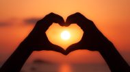 Hands forming a heart shape in a sunset sky